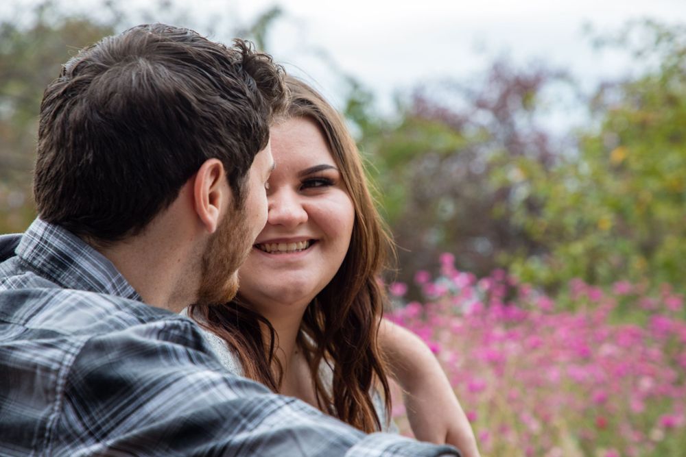 A couple shares a romantic moment outdoors with blooming pink flowers in the background.
