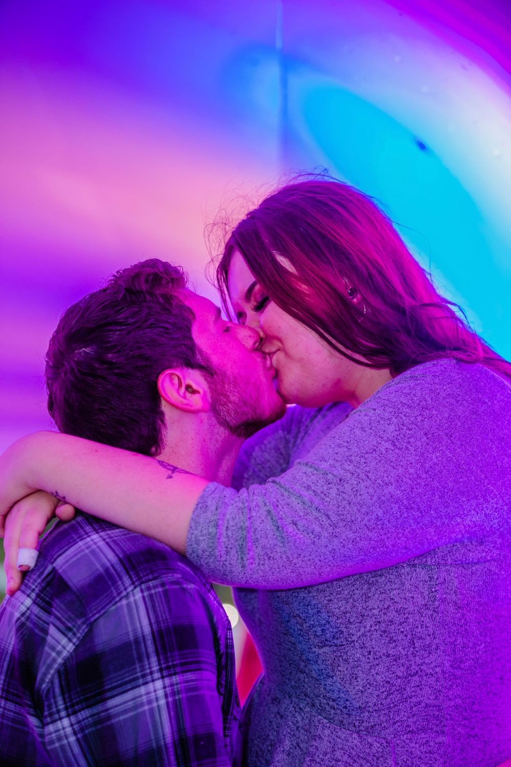 A romantic couple sharing an intimate kiss under vibrant purple and blue lighting.