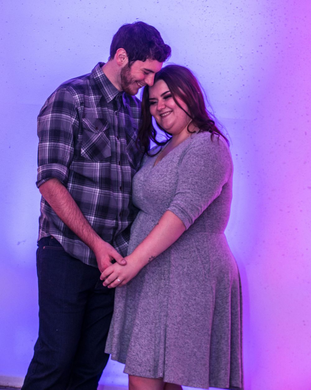 A romantic couple shares an intimate moment under purple lighting, with him in plaid and her in a gray dress.