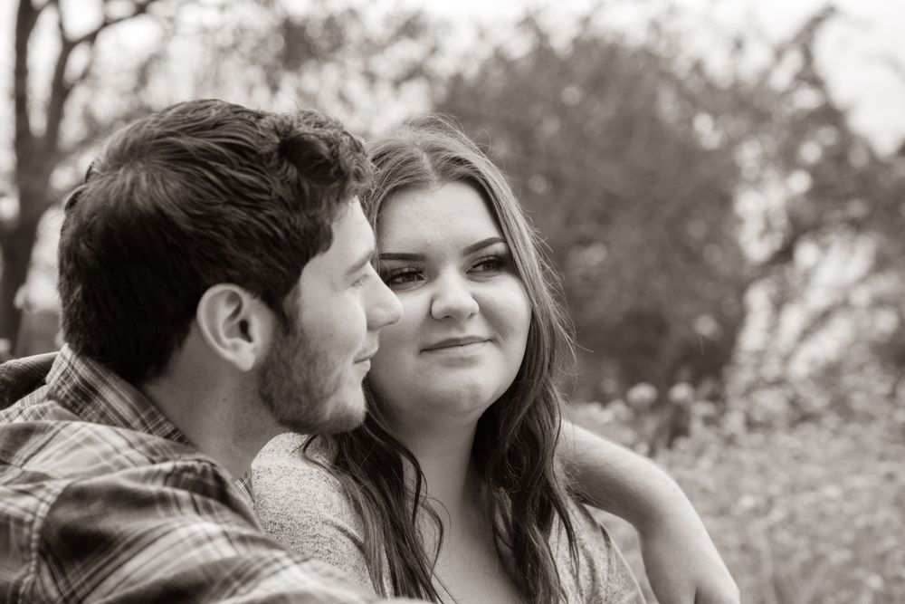 Black and white photo of a couple sharing a romantic moment outdoors with trees in background.