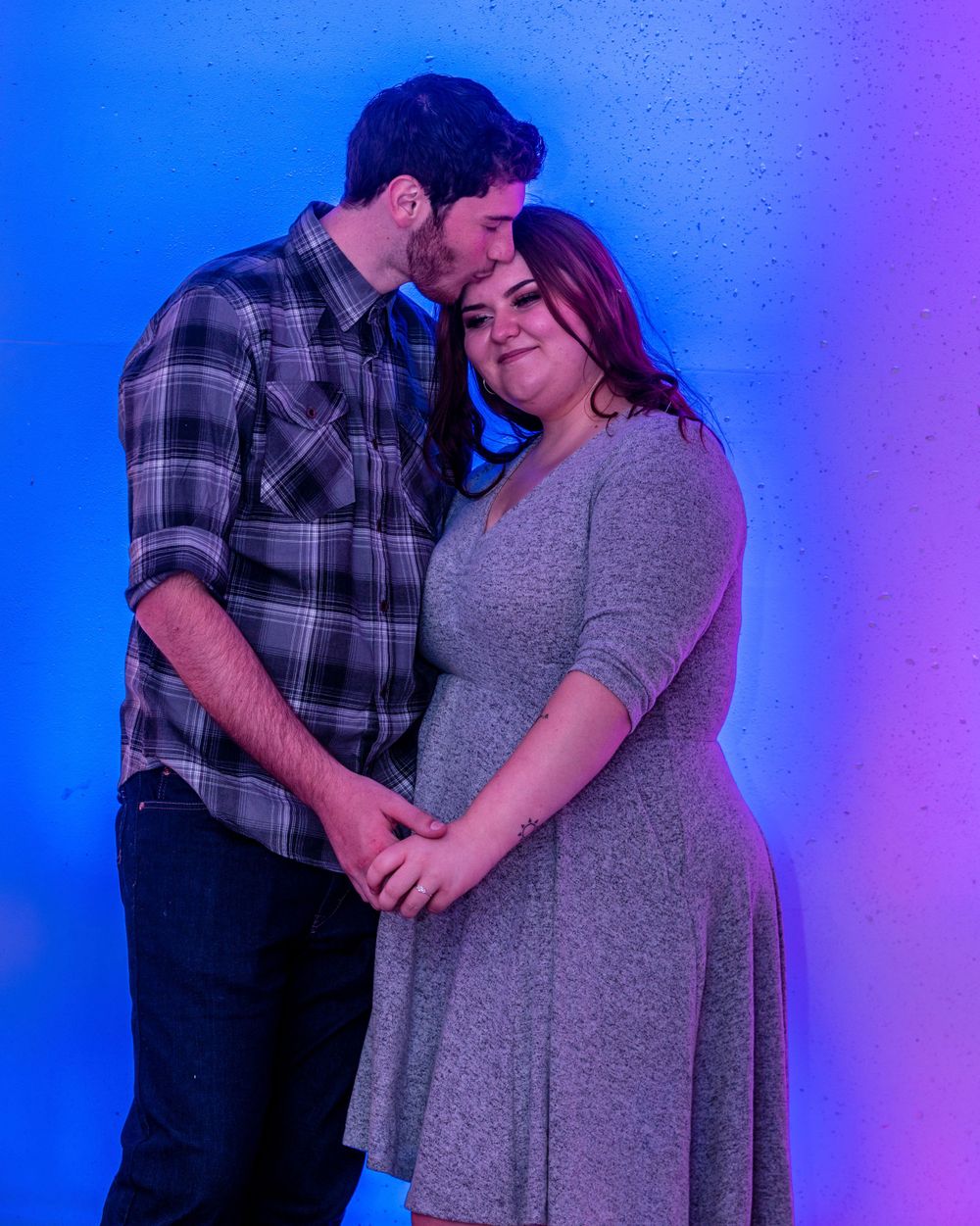 A romantic couple embraces against a vibrant blue and purple gradient background in a moody studio setting.