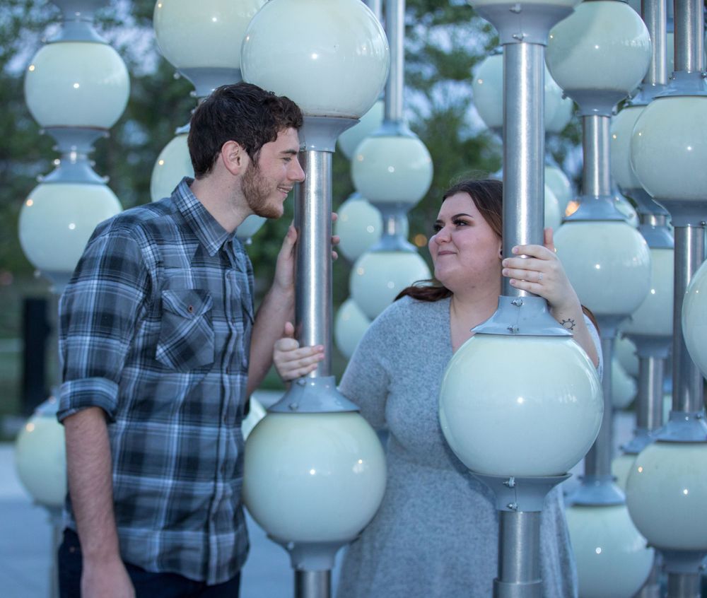 A couple poses together near an artistic display of large white globe-shaped lights mounted on poles.
