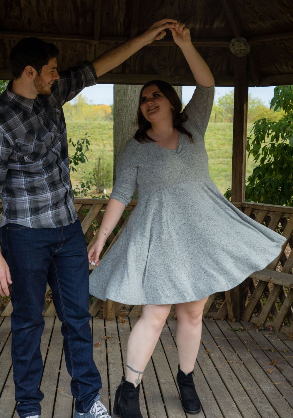 Two people dance together on a wooden deck gazebo with a green field visible in the background.