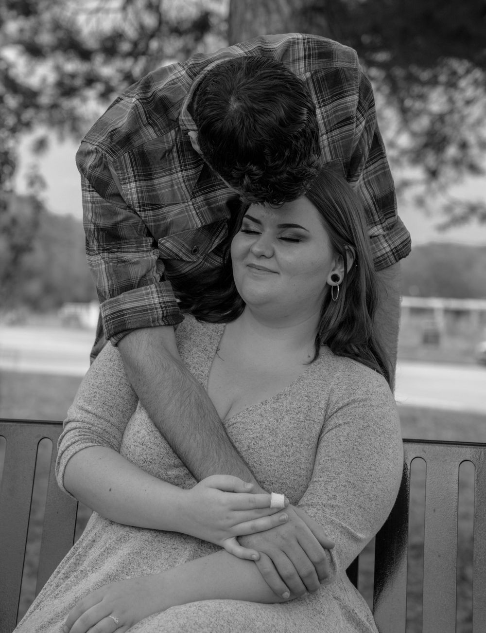 Black and white romantic photo of a couple embracing on a park bench, capturing a tender moment together.