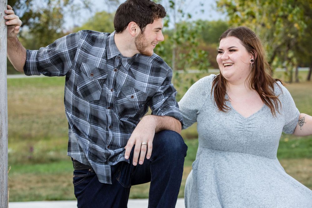 Two people share a playful conversation while sitting outdoors on a white surface on a sunny day.