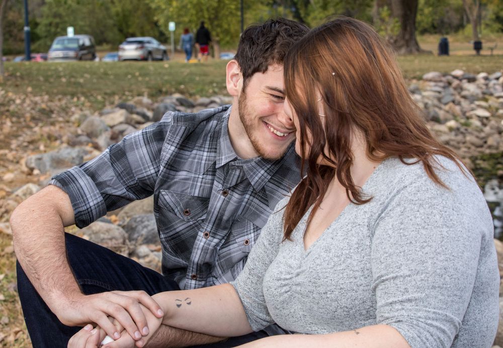 A couple shares an intimate moment outdoors sitting on rocks while enjoying a sunny day together.