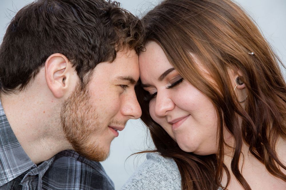 A romantic couple sharing an intimate moment touching foreheads while smiling warmly at each other.