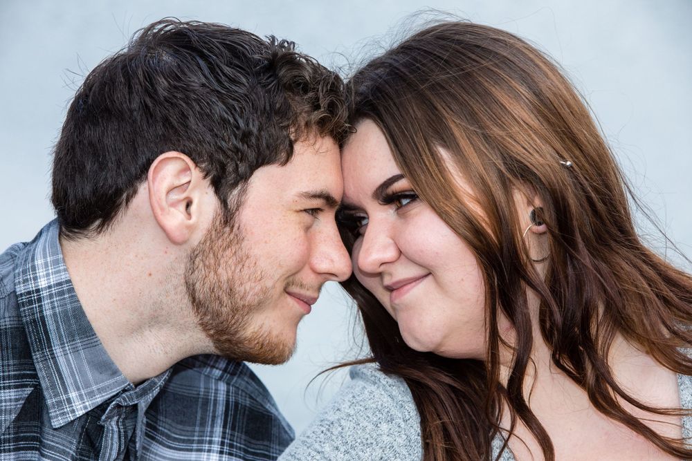 A young couple touching foreheads intimately while sharing a tender romantic moment against a light background.