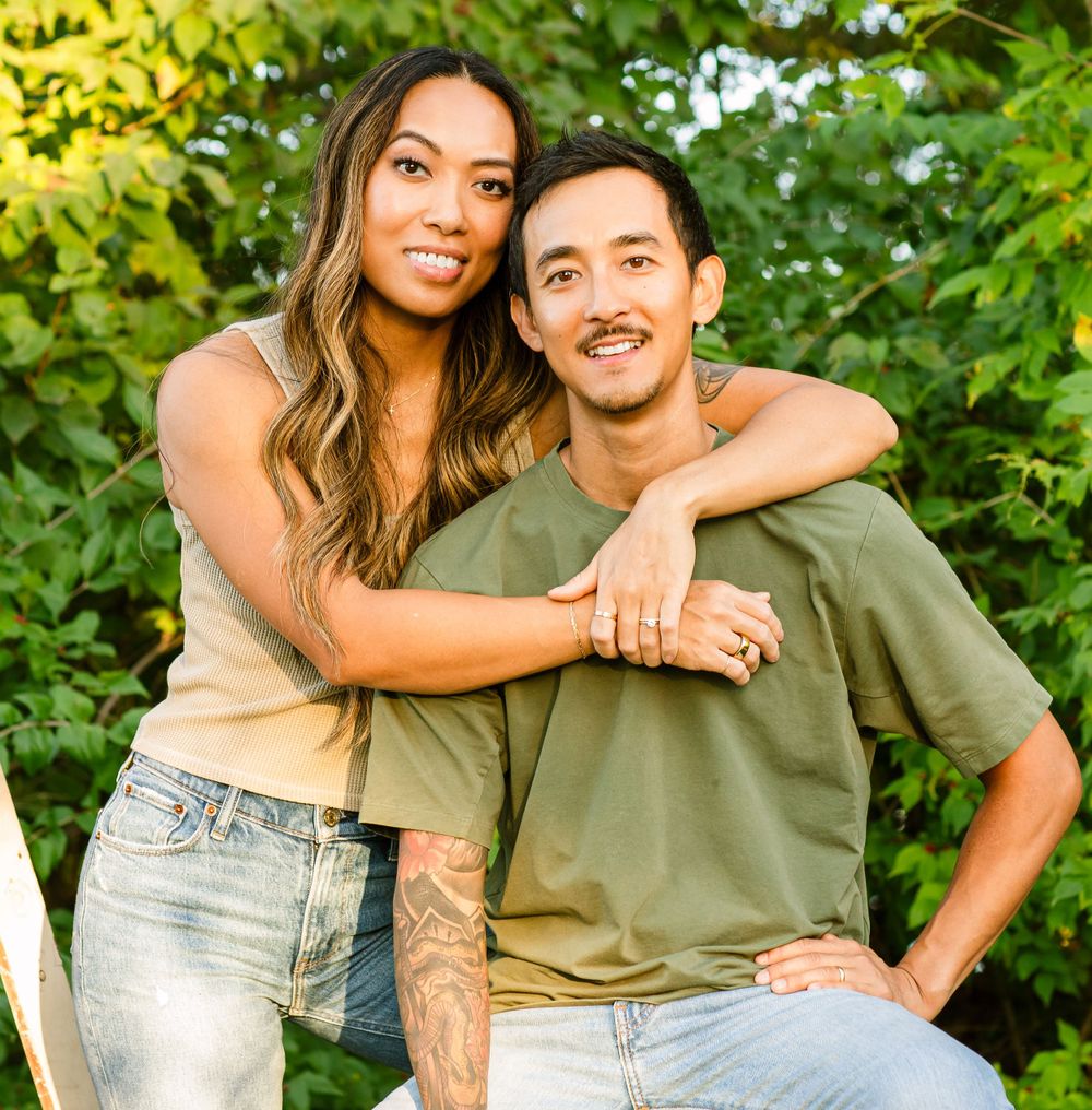 Happy couple sitting together outdoors in green t-shirts against lush foliage background.