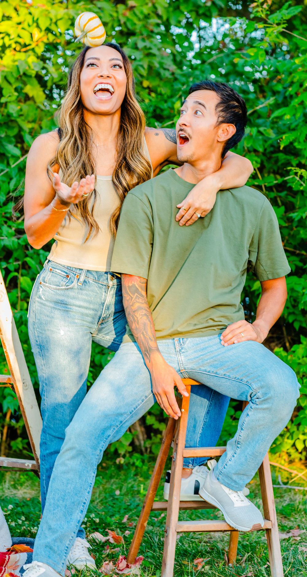 A joyful couple shares a candid laughing moment together outdoors against green foliage while wearing casual clothing.