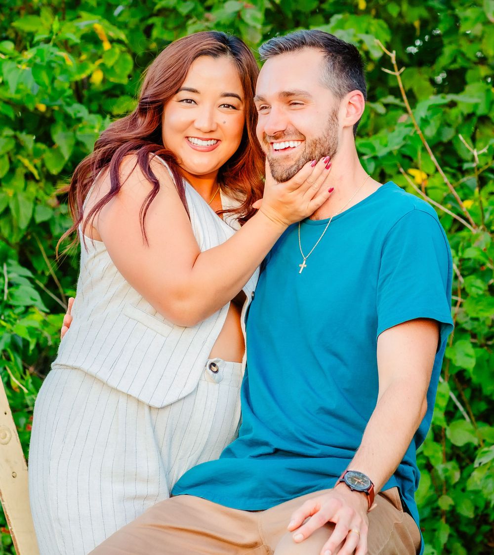 A happy couple sharing a joyful and playful moment together against a lush green backdrop.