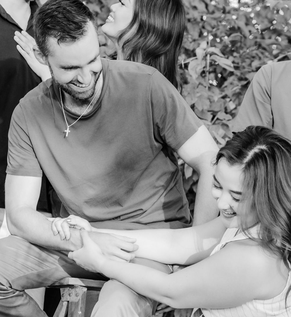 A couple shares a lighthearted moment together while seated outdoors, both laughing and enjoying each other's company.
