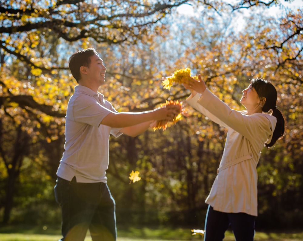 A couple play with autumn leaves together in a sunlit park during golden hour.
