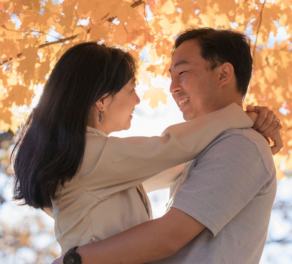 A romantic couple embraces outdoors against a backdrop of warm autumn foliage during golden hour.