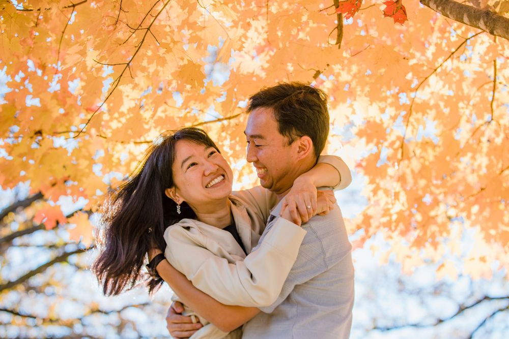 Happy couple embracing under vibrant orange autumn maple leaves during a romantic outdoor photo session.