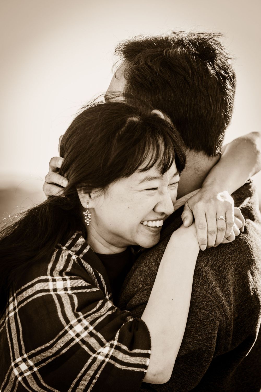 A candid sepia-toned photograph captures a joyful intimate moment between two people embracing and laughing.
