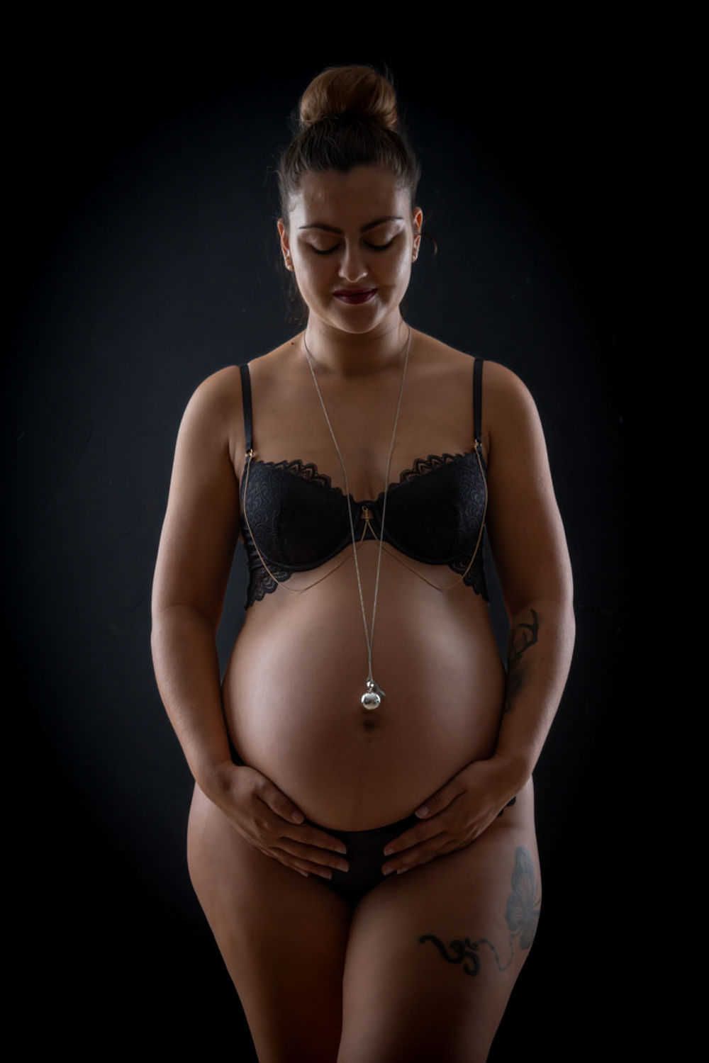 Photo de maternité artistique montrant une future maman en lingerie noire sur fond sombre avec un collier délicat.
