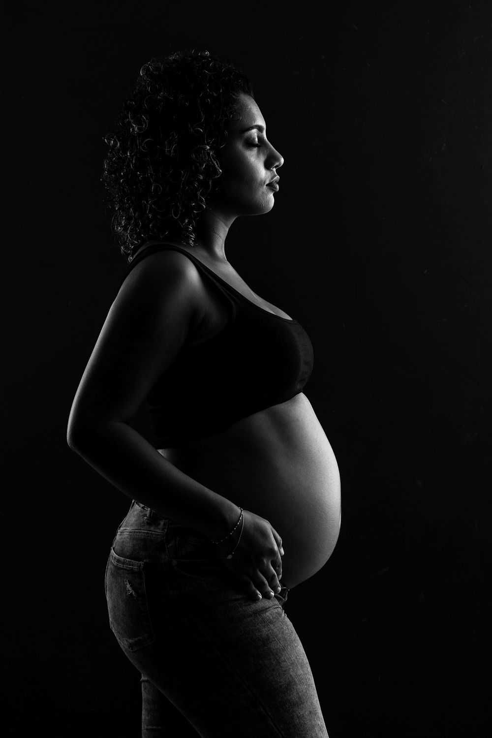 Silhouette de profil de maternité dramatique en noir et blanc montrant la silhouette d'une femme enceinte sur un fond sombre.