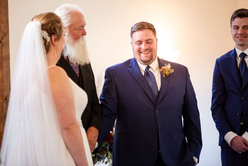 A wedding ceremony takes place with people in formal attire including a bride in white and navy suits. Iowa City wedding photographer.