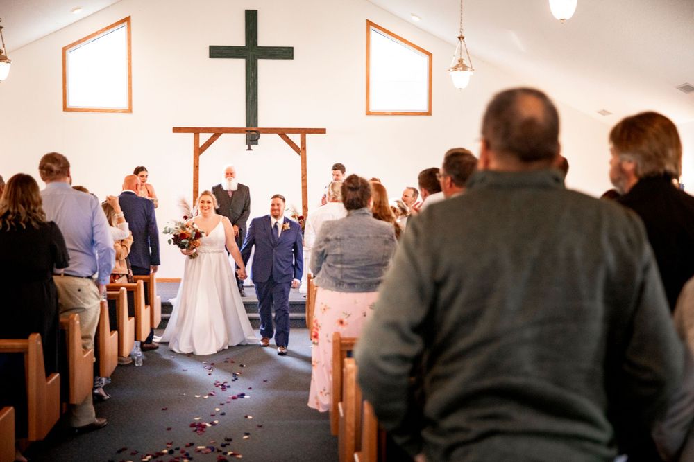 A couple walks down the church aisle after their wedding ceremony as guests look on from wooden pews. Iowa City wedding photographer.