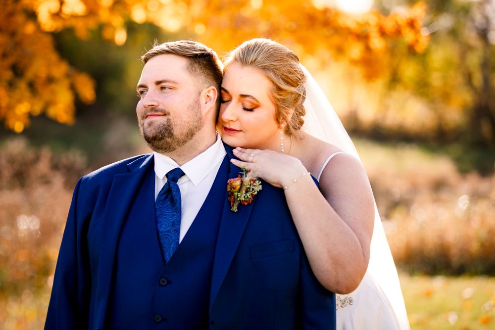 A couple shares a romantic moment outdoors during autumn with vibrant orange foliage in the background. Iowa City wedding photographer.