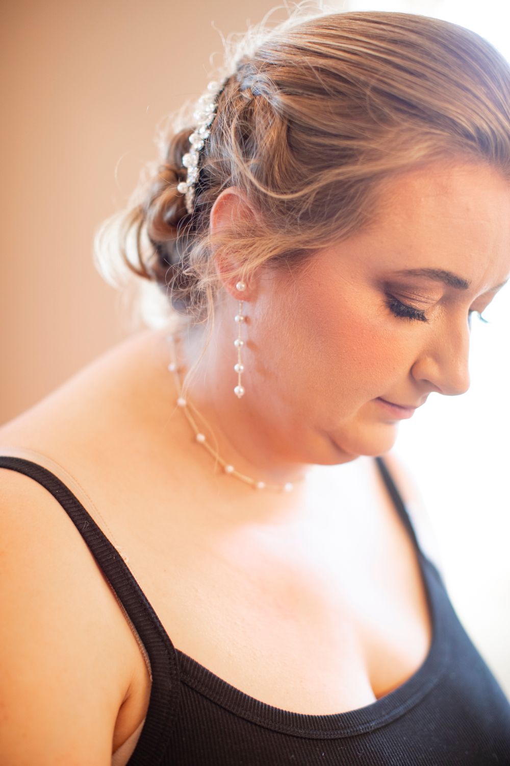 Light falls softly on a bride looking down, wearing delicate dangle earrings in warm natural lighting.   Iowa City wedding photographer.