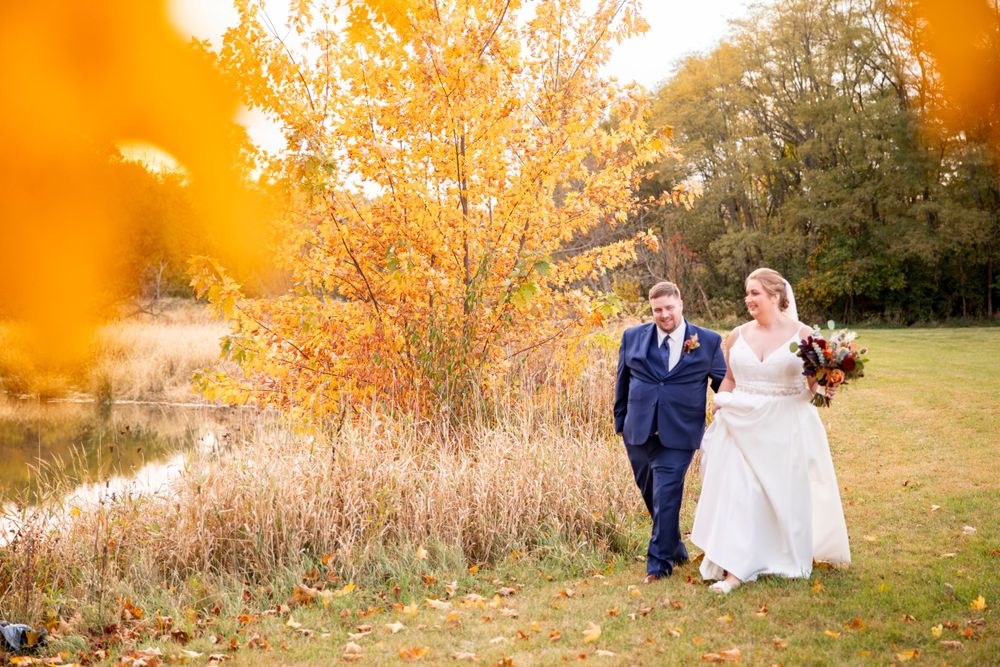 Wedding couple walking together on an autumn day by a pond surrounded by golden foliage and warm sunlight.  Iowa City wedding photographer.
