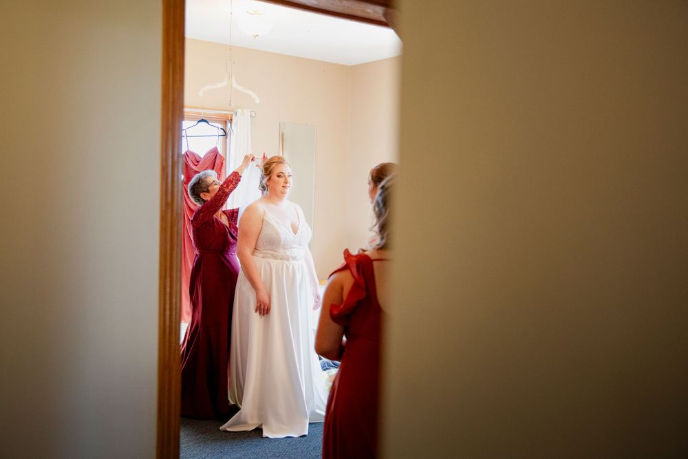 Elegant bridal party preparing in a room with red bridesmaid dresses and a flowing white wedding gown. Iowa City wedding photographer.