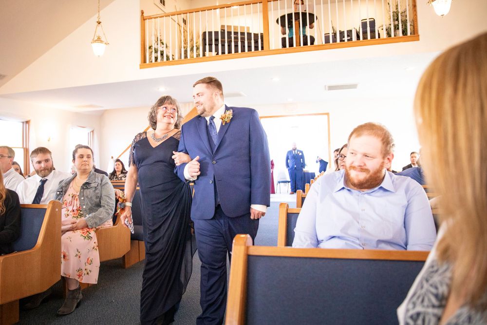 People gather inside a church during a formal event, with wooden pews and an organ loft in the background. Iowa City wedding photographer.