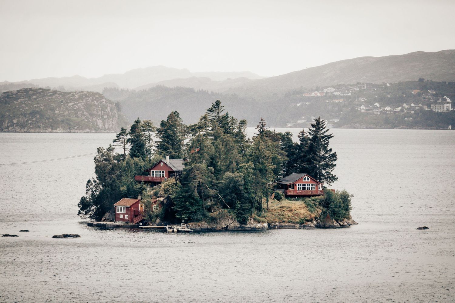 Small island covered in evergreen trees with red cottages nestled among the foliage.