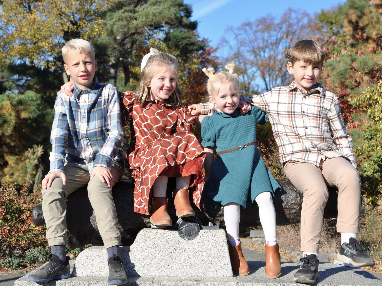 Four cousins sit together on a rock in Central Park, NYC, during a family photo session, surrounded by nature.