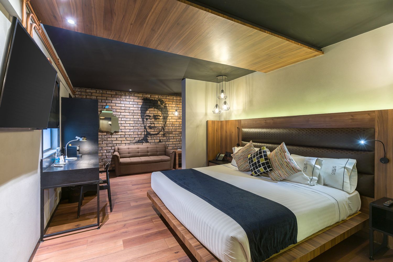 Modern hotel room interior with wooden ceiling, brick accent wall, and sleek desk area. Cadillac Hotel Boutique CDMX.