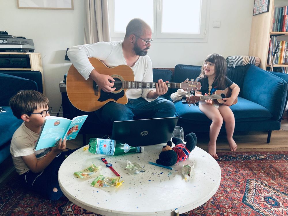 Family gathering in living room with guitar and crafts on coffee table.
