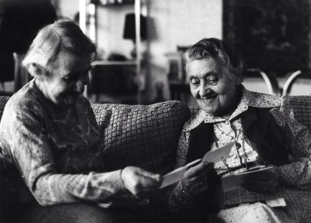 Vintage black and white photo of elderly pair reading together on couch.