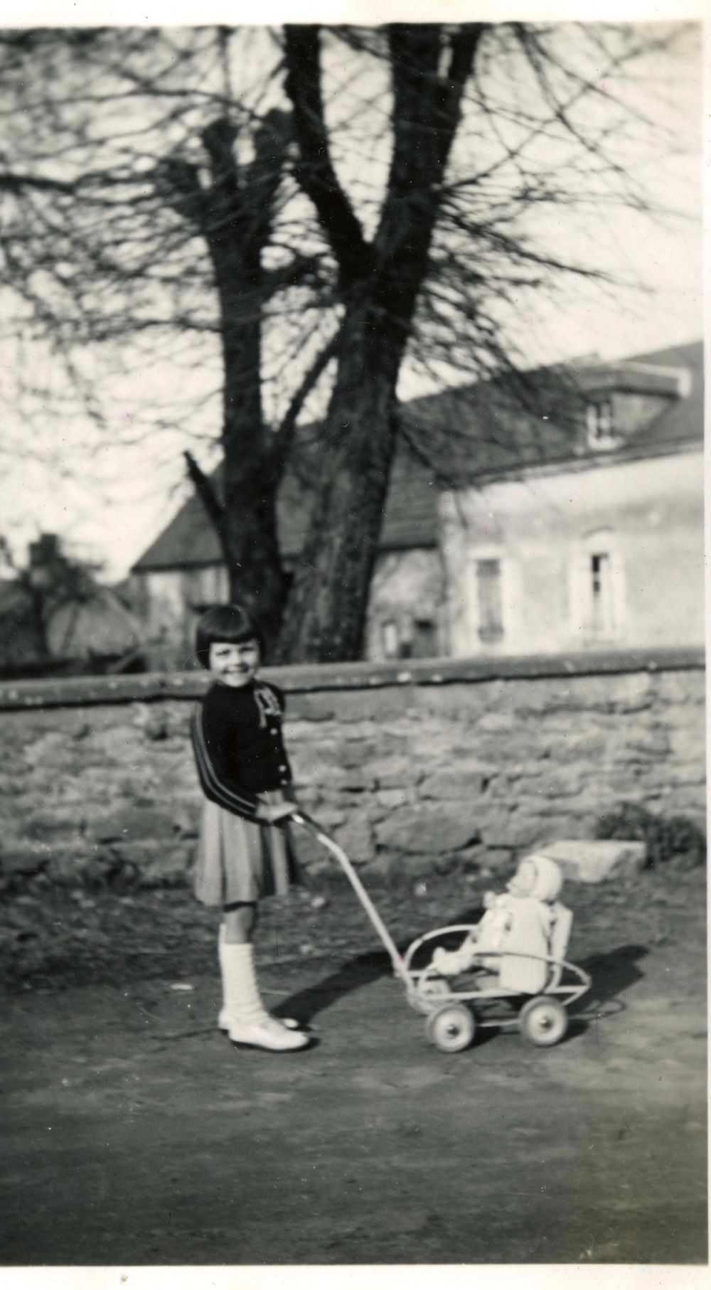 Vintage black and white photo of child pulling toy wagon outdoors.