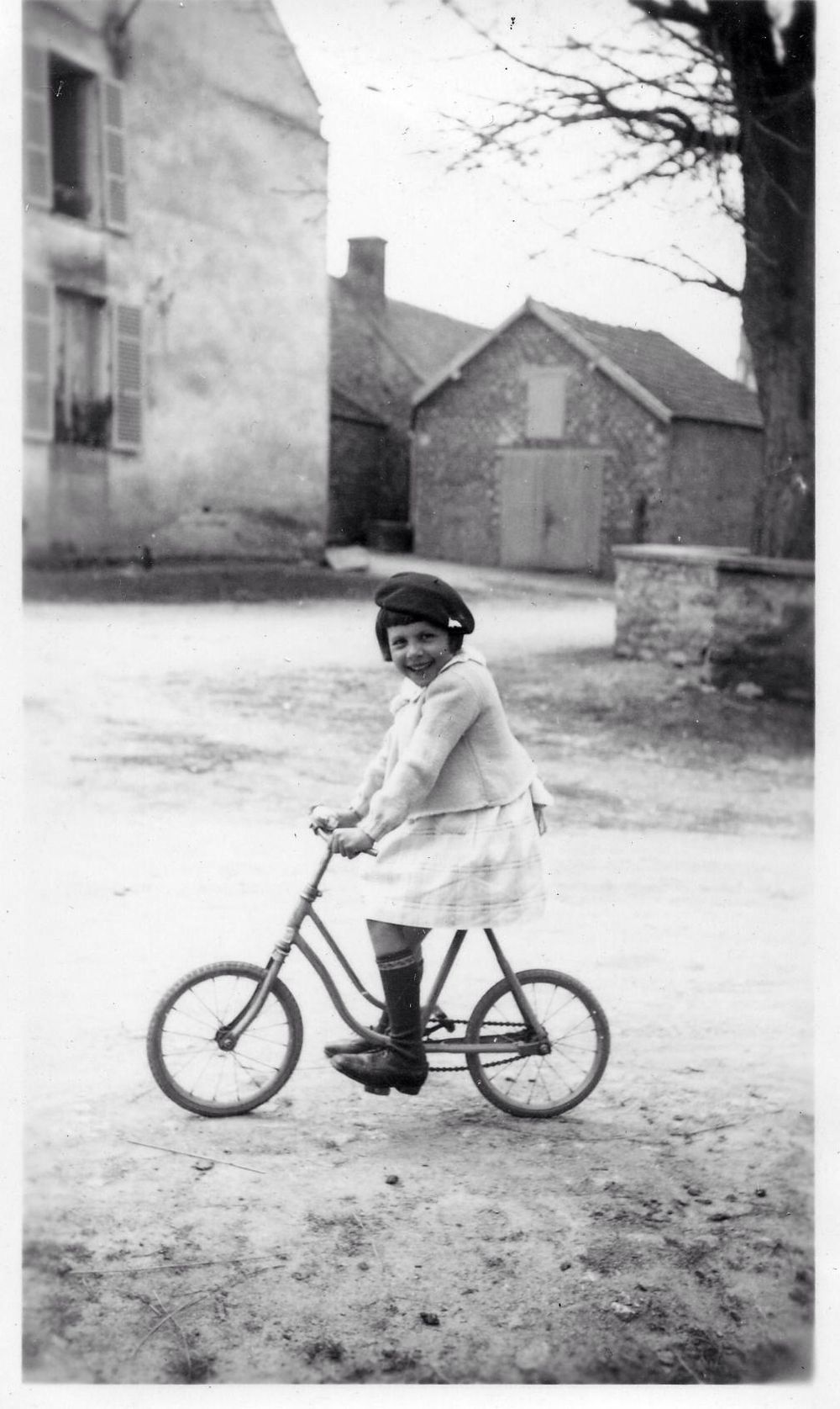Vintage black and white photo of child on bicycle in front of stone buildings.