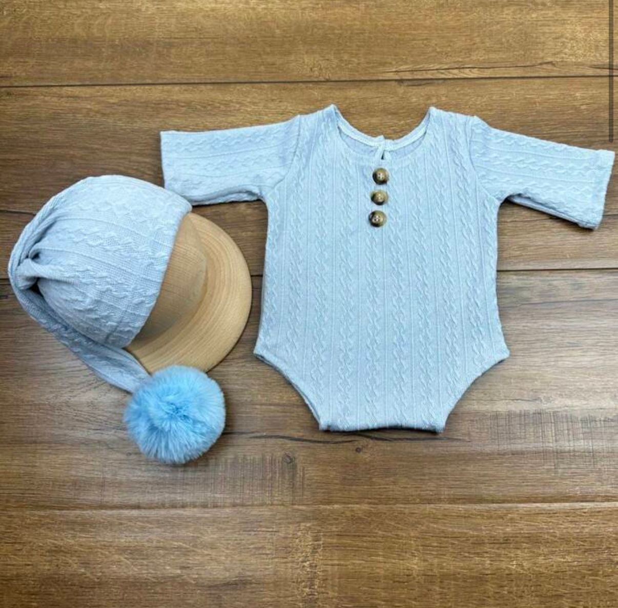 Light blue quilted baby romper with matching pom pom hat on wooden surface.