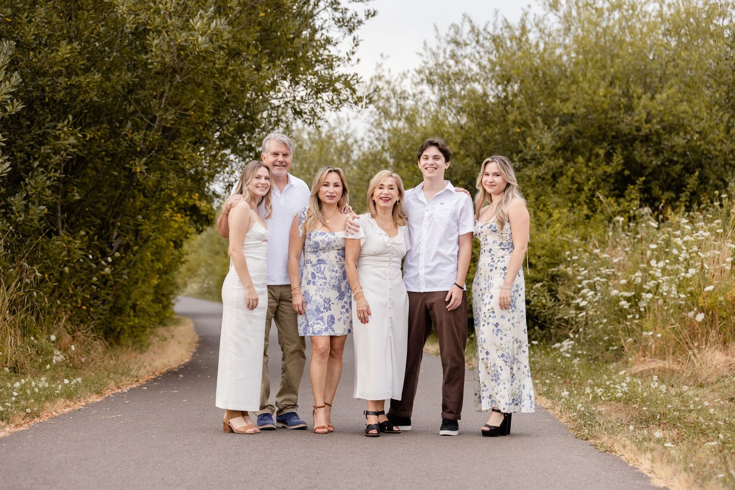 A happy family poses together on a sunny path surrounded by wildflowers and greenery.