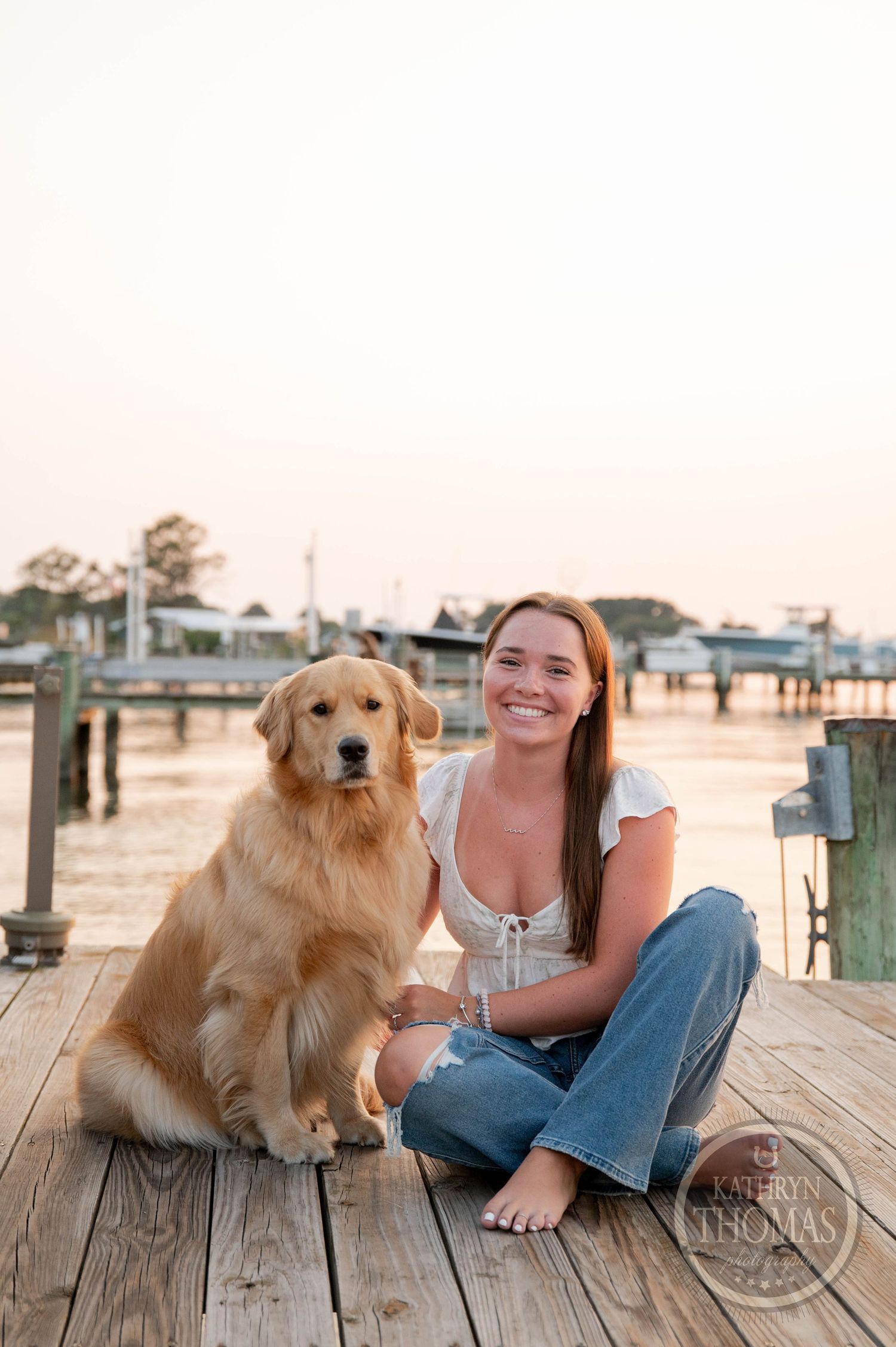 Golden Retriever and person sitting together on wooden dock at sunset.