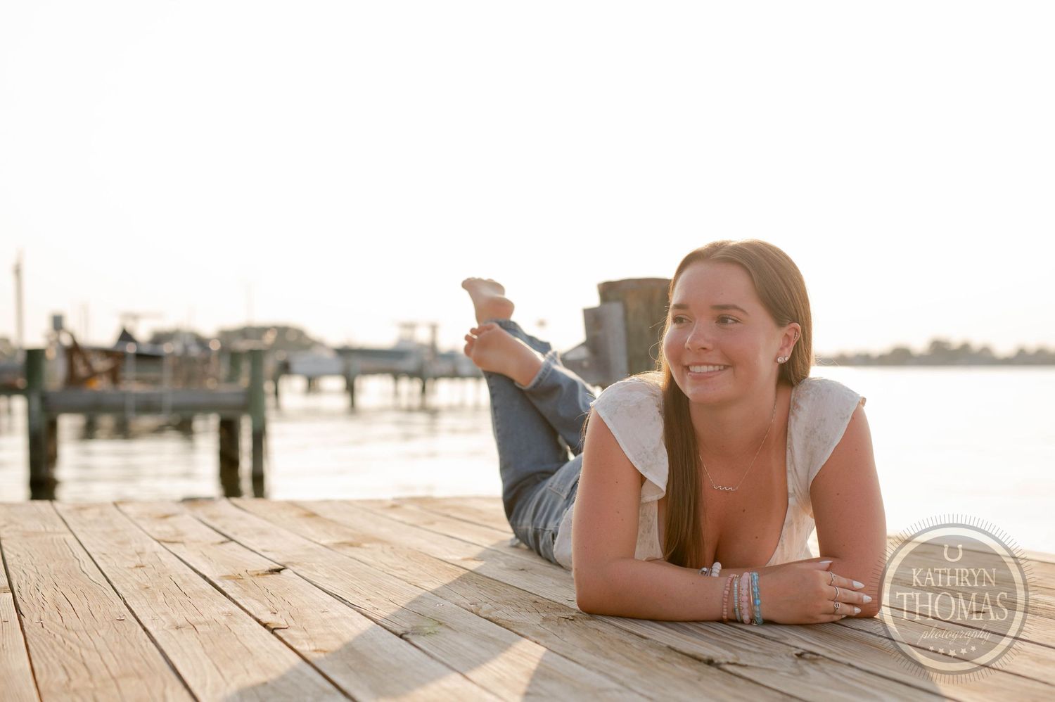 Person relaxing on a wooden dock by the water during sunset.