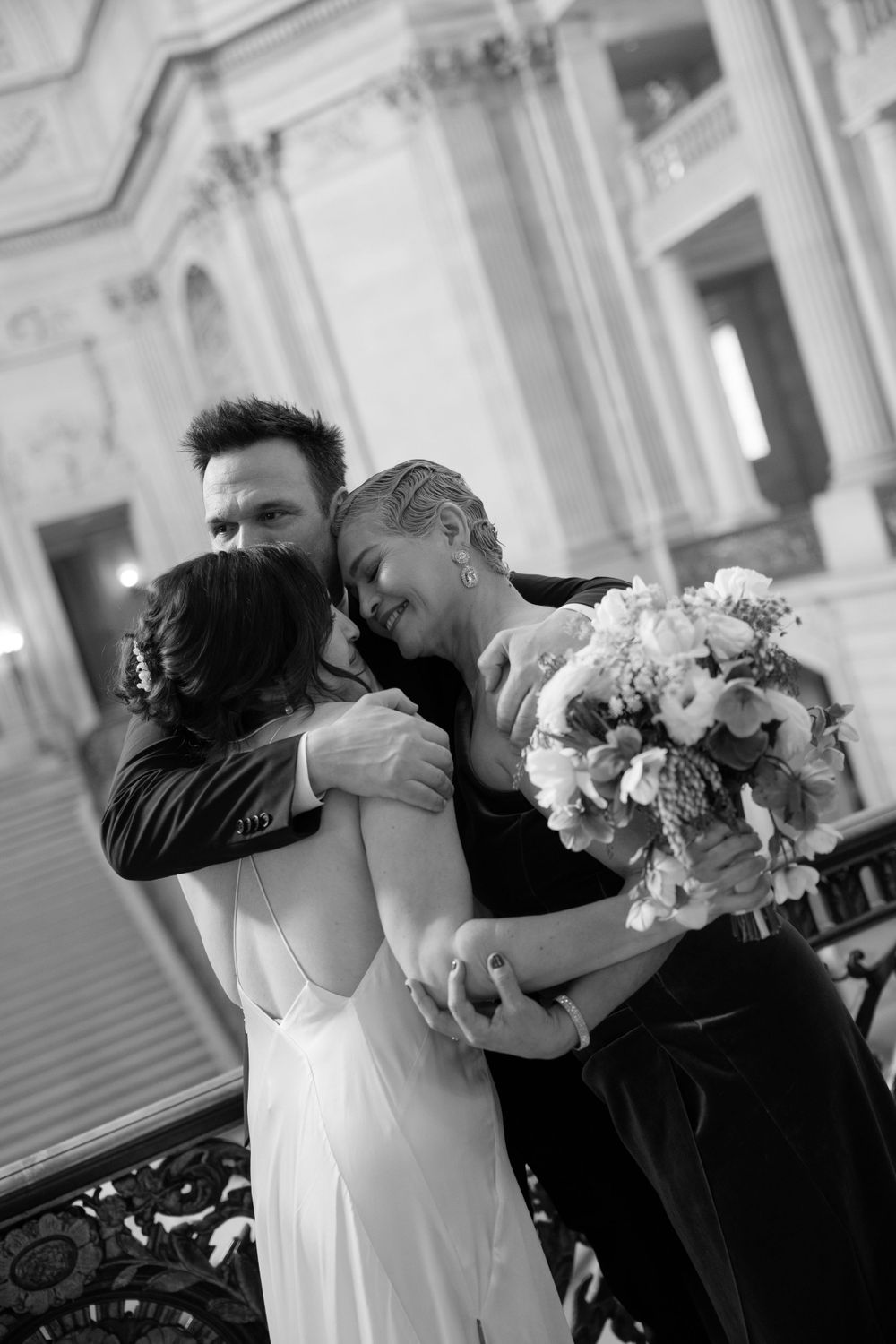 A romantic black and white wedding photo showing an embrace and bouquet of flowers on an elegant balcony.