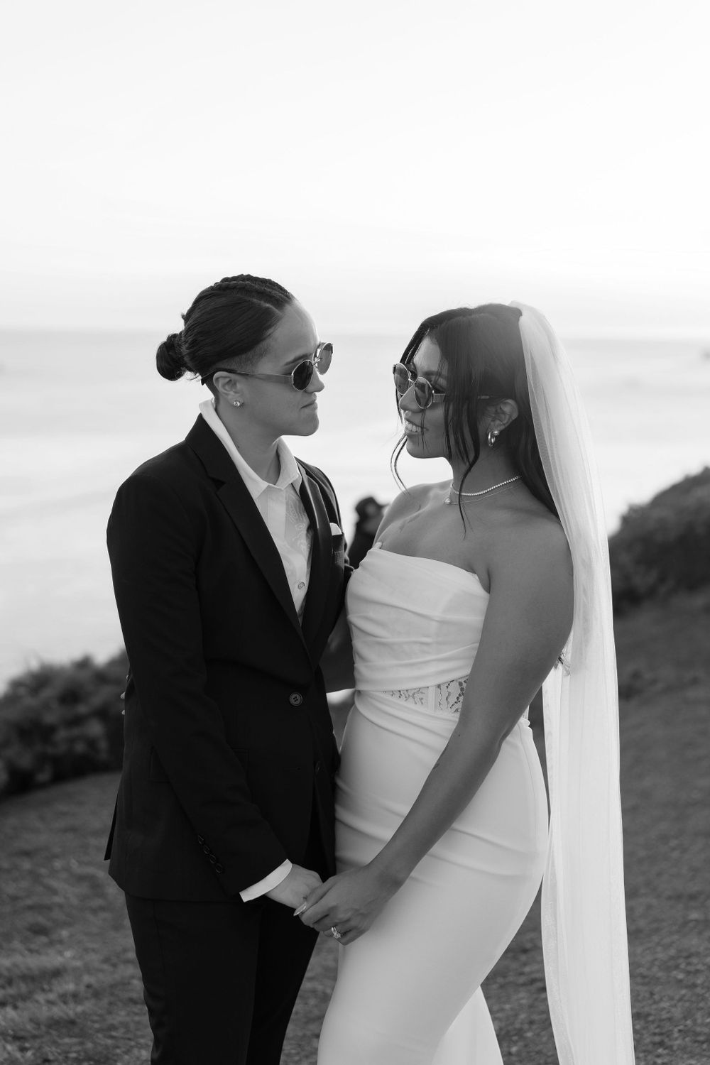 Black and white wedding photo of a couple sharing a romantic moment on a hilltop overlooking the ocean.