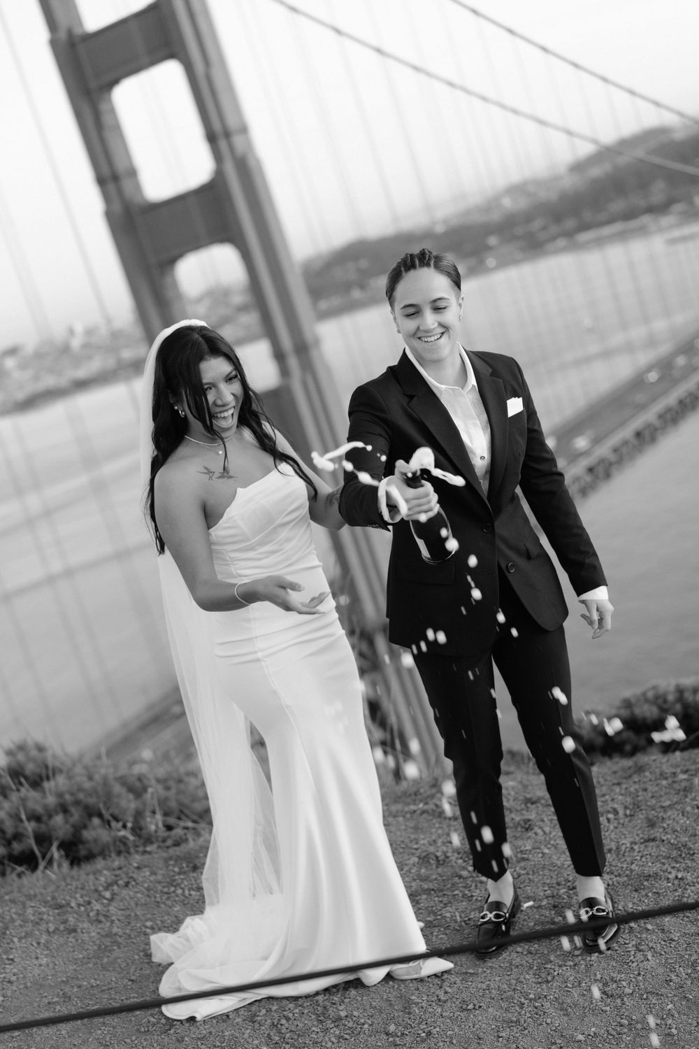 A happy couple in wedding attire laugh and celebrate near the Golden Gate Bridge in San Francisco.