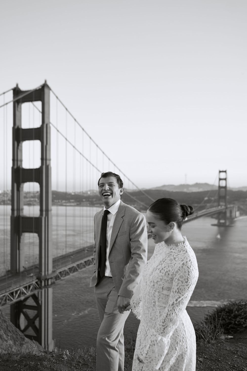 A black and white photo of a couple sharing a joyful moment near the Golden Gate Bridge in San Francisco.
