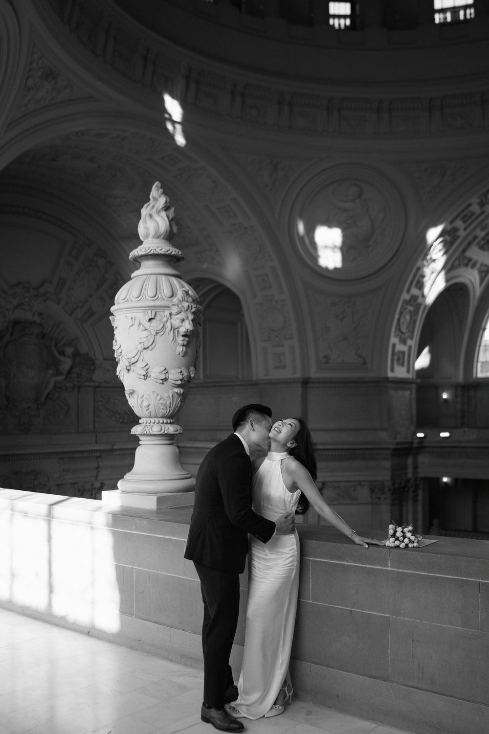 A romantic black and white wedding photo captured in an ornate historic building with classical architectural details.