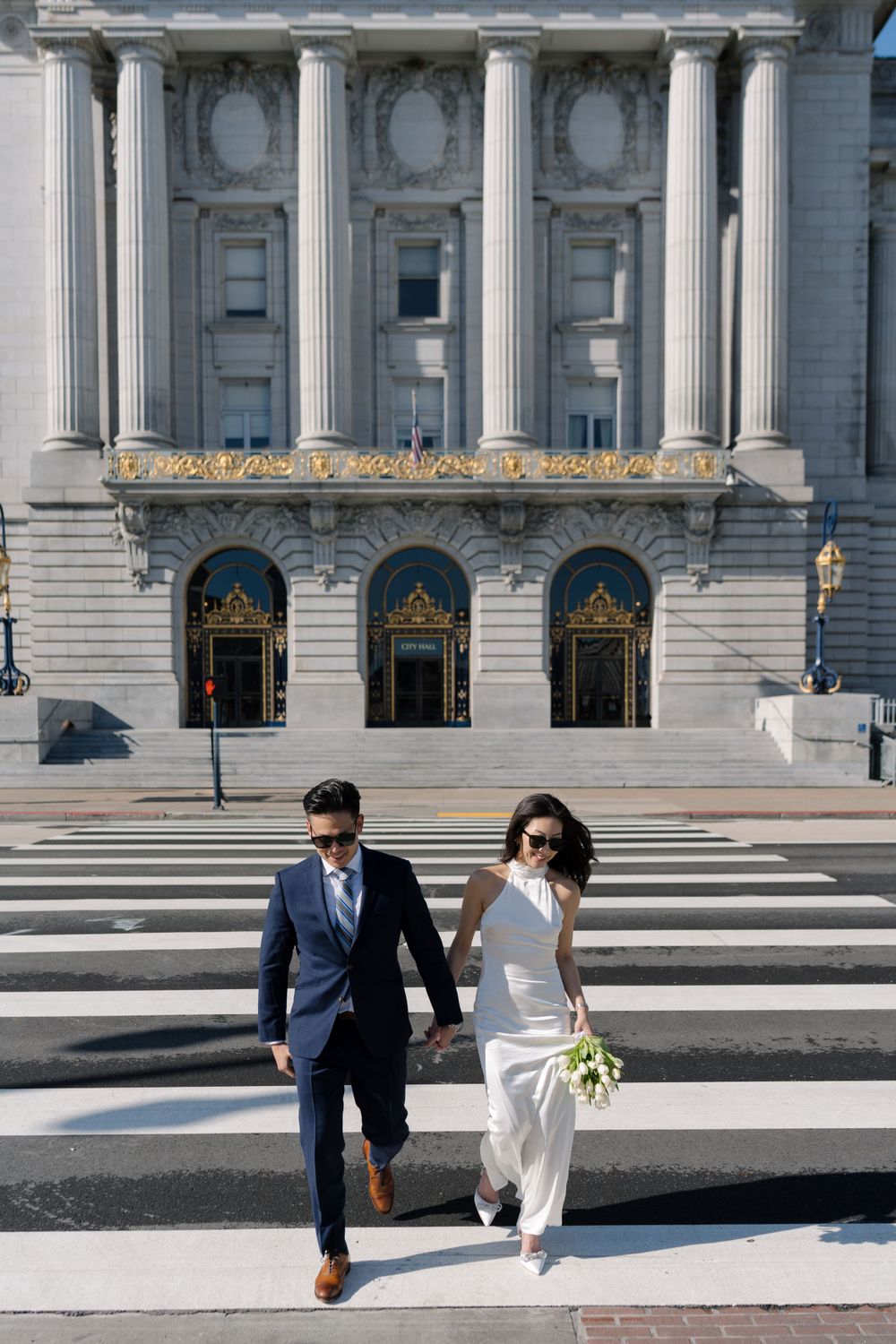 A couple crosses a crosswalk in front of the classic architecture of San Francisco City Hall.