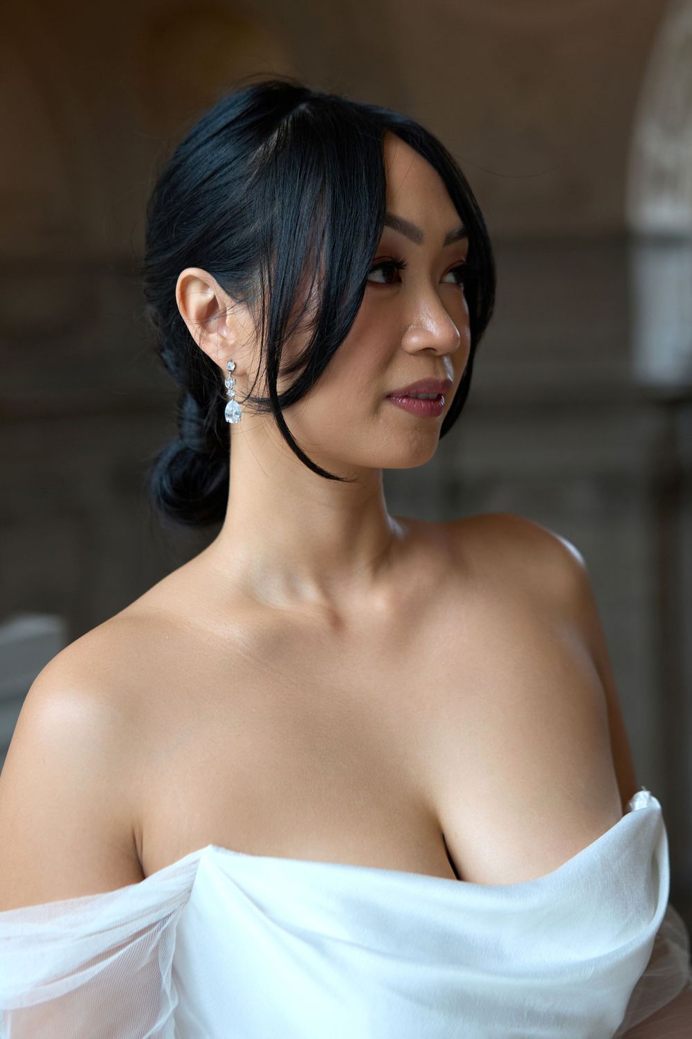 Portrait of someone in an elegant off-shoulder white dress with dark hair styled in a romantic updo, looking to the side.