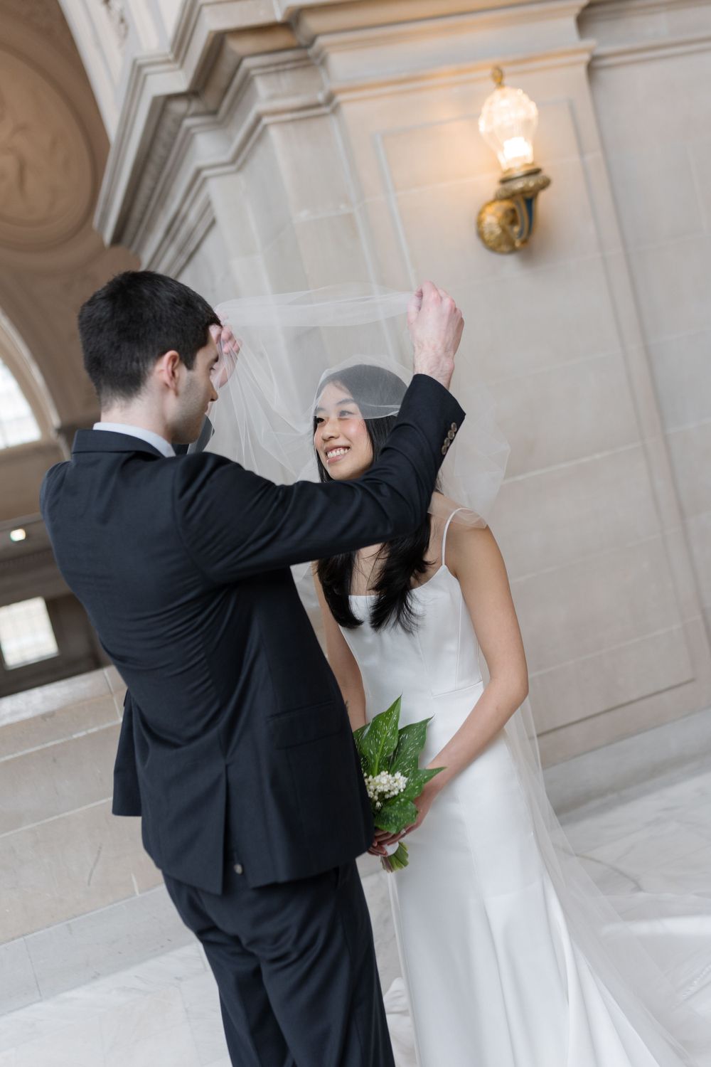 A happy couple shares their first dance together in a bright elegant hallway with classical architecture and wall sconces.