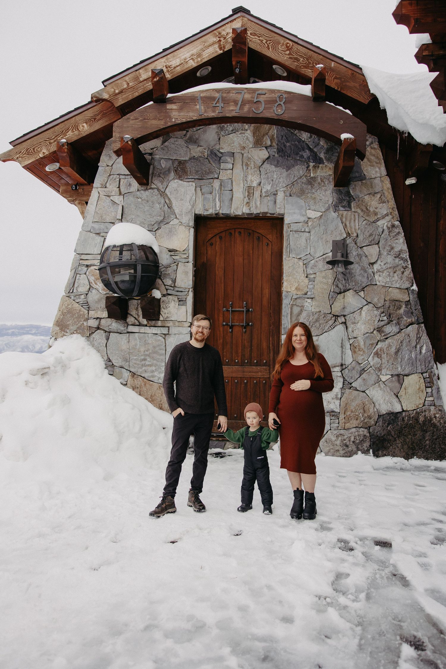 A family stands in front of a rustic stone building entrance with wooden beams in a snowy winter setting.