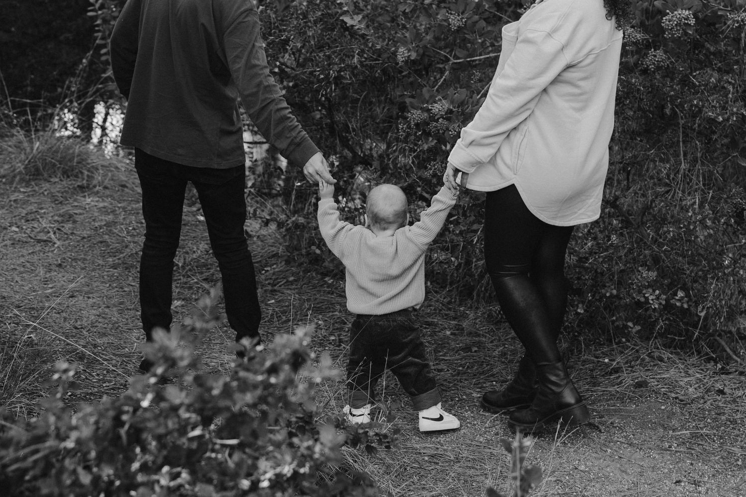 Small figure holds hands with two others while walking through nature in black and white.